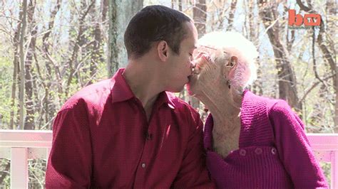 An Older Couple Kissing Each Other While Sitting On A Bench In Front Of