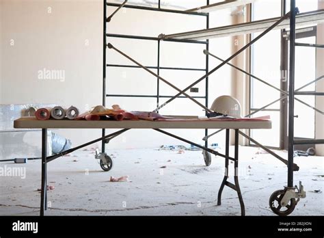 Table With Blueprints And Hardhat In Front Of Scaffold In Construction