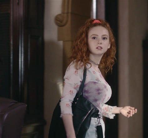 A Woman With Red Hair Is Standing In A Room And Looking At The Camera While Wearing A Black Purse