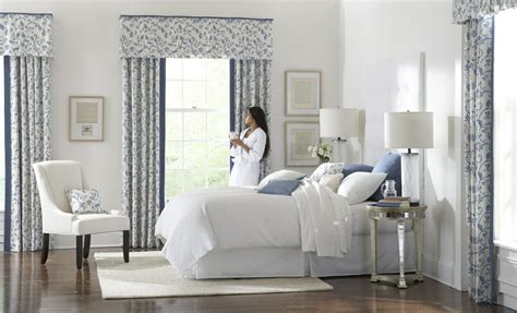 Cottage bedroom features three windows dressed in white roman shades placed over a decorative oar lining a wall above a bed dressed in white bedding and taupe pillows flanked by white linen nailhead open nightstands. Window Treatment Ideas for the Bedroom - 3 Blind Mice
