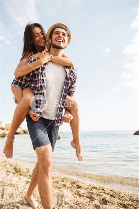Handsome Smiling Young Man Giving Piggy Back Ride To His Girlfriend At