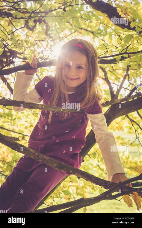 Portrait Of Smiling Little Girl Climbing In An Autumnal Tree Stock