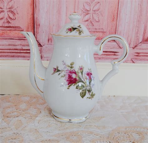 A White Tea Pot With Pink Flowers Painted On The Side And Gold Trimmings