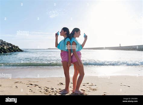 Twin Sisters In Matching Outfits Standing Back To Back With Squirt Guns At Beach Stock Photo Alamy