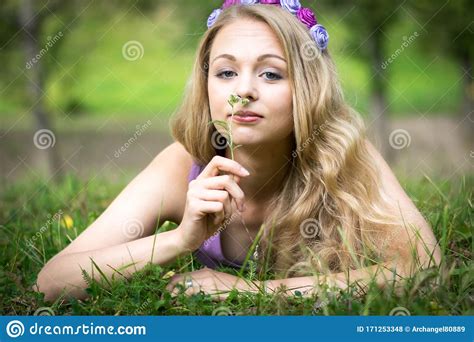 Beautiful Blonde Girl Lying On The Grass And Smelling A Flower Stock