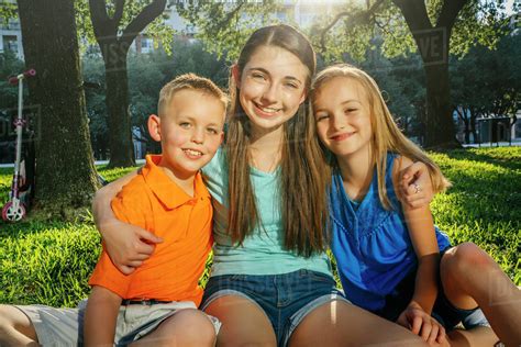 Portrait Of Smiling Caucasian Brother And Sisters Hugging In Park