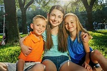 Portrait of smiling Caucasian brother and sisters hugging in park ...