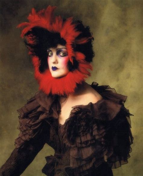 A Woman Wearing A Red And Black Mask With Feathers On Its Head Is