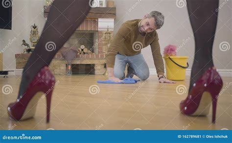 Joyful Caucasian Husband Or Henpecked Washing The Floor On The Knees And Laughing Young Man