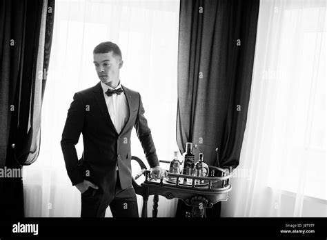 Portrait Of A Groom Posing For His Wedding Photo Session In His Room Standing Next To A Table