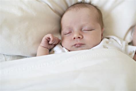 A Sweet Newborn Baby Girl Sleeping In White Bed With Clock On The Side