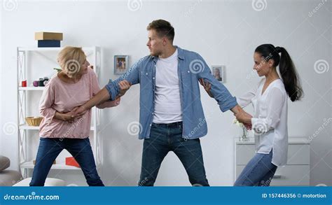 Mother And Wife Pulling Young Man In Different Directions Conflict In