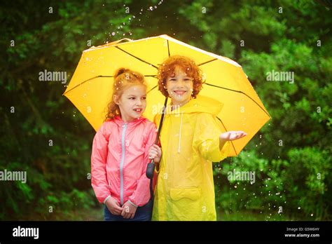 Brother And Sister Stand Together Under A Big Yellow Umbrella The