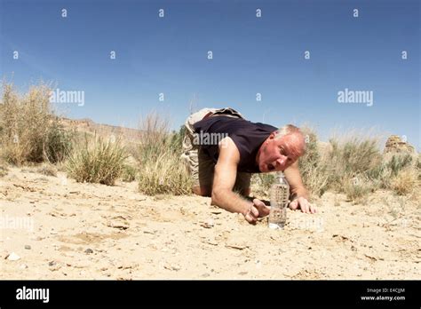 Man Reaching For Bottle Of Water While Crawling On Desert Floor Stock