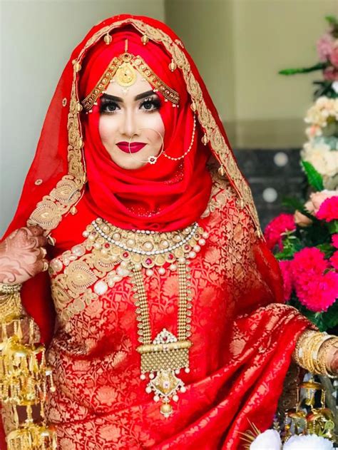 A Woman In A Red And Gold Bridal Outfit Posing For The Camera With Flowers Behind Her