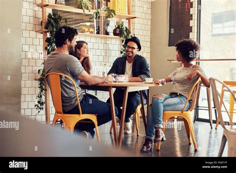 Young People Sitting At A Cafe Table Group Of Friends Talking In A