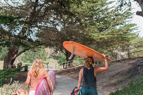 Two Women Carrying Surfboards Along A Pathway By Stocksy Contributor Briana Morrison Stocksy