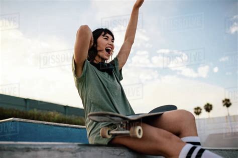 Smiling Urban Young Woman Sitting On Skateboard Ramp In Skate Park