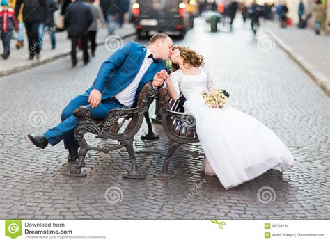 Close Up View Of The Kissing Newlyweds While Sitting On The Bench