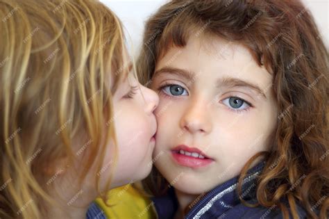 Белокурая маленькая девочка целует дочь голубыми глазами Премиум Фото
