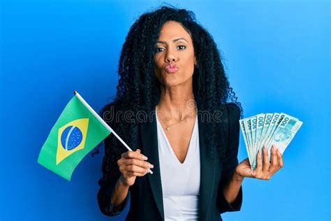 middle age african american woman holding brazil flag and real banknotes looking at the camera