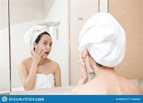 Happy Young Asian Woman Applying Face Lotions While Wearing A Towel And Touching Her Face In