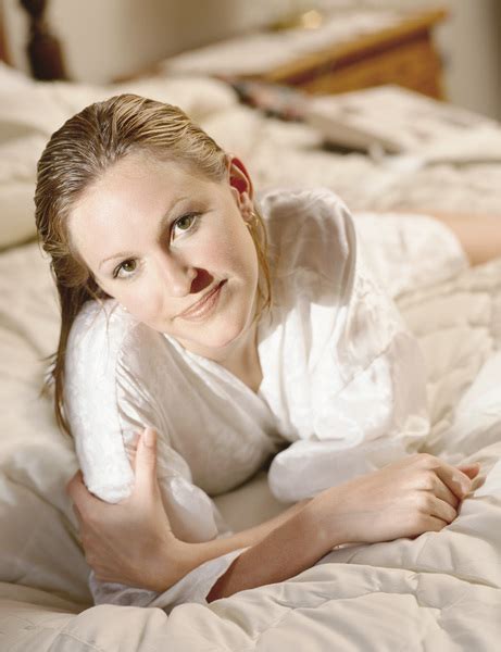blonde caucasian woman lying or laying on a bed in a white bathrobe after having just showered