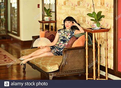 A Wealthy Cheongsam Wearing Chinese Woman Relaxes On A Rattan Daybed In