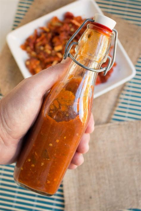 A Hand Holding A Bottle Filled With Sauce On Top Of A Table Next To A