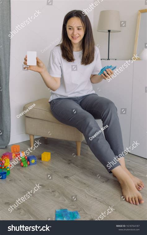 Portrait Of Beautiful Nanny Sitting In Cozy Playroom And Showing Mock Up Of Educational Cards