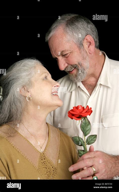 a handsome mature husband surprising his wife with a red rose vertical view over black stock
