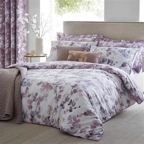 A Bed With Purple And White Comforters In Front Of A Window Covered By