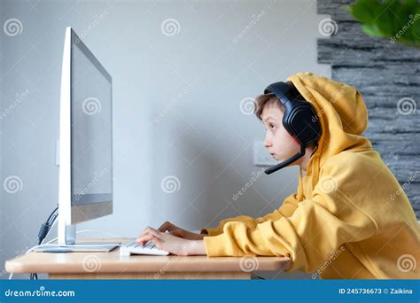 Teenage Boy In Headphones Uses Computer At Home At A Distance Learning