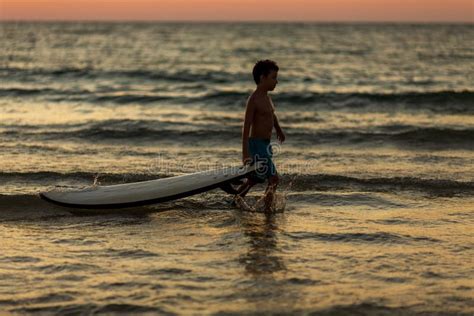 Silhouette De Un Niño Corriendo a Lo Largo De La Playa Con Una Tabla De Surf Al Atardecer Foto
