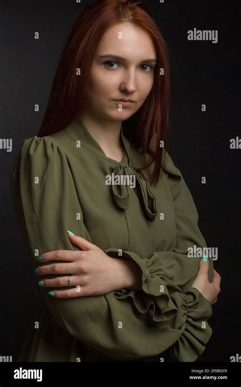 Ginger Young Woman On Black Background In A Green Shirt Crossed Her