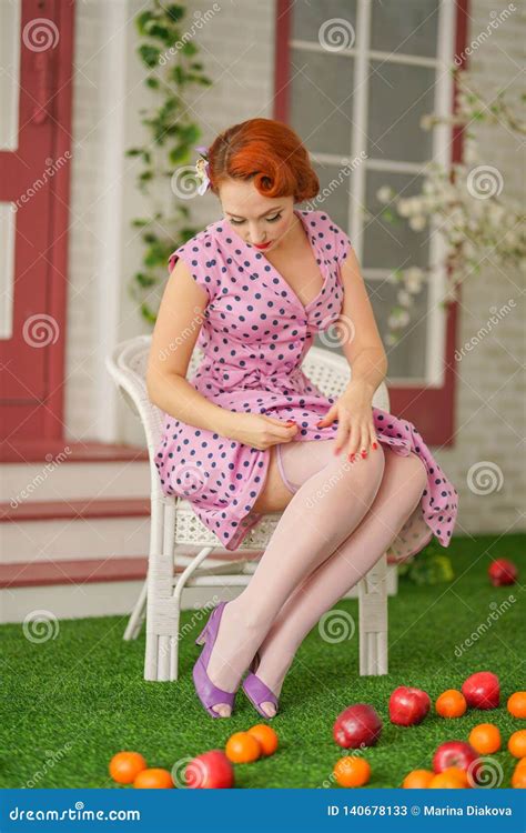 Beautiful Redheaded Pin Up Girl In Pink Polka Dot Dress And Vintage Stockings Posing Near The
