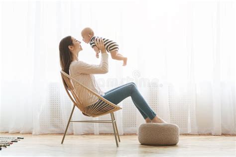 Mother Sitting In Chair And Lifting Her Newborn Child Up Stock Photo