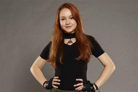 A Woman With Long Red Hair And Black Shirt Posing For A Photo In Front Of A Gray Background