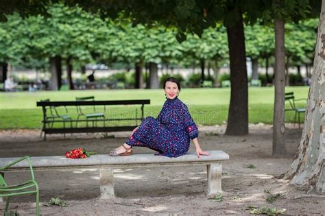 Attractive Woman In A Blue Dress Sitting In The Park Stock Photo