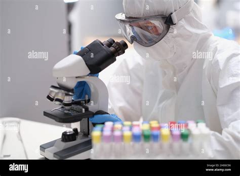 Scientist In Protective Suit And Mask Looks Through Microscope Stock