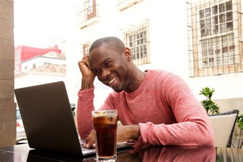 Happy Black Guy Sitting At Outdoor Cafe With Laptop Computer Stock