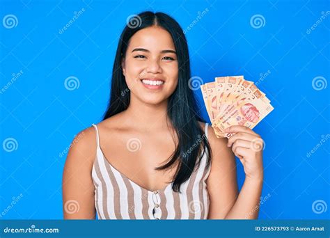 Young Beautiful Asian Girl Holding Mexican Pesos Looking Positive And