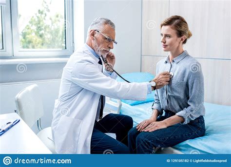 Serious Mature Male Doctor Examining Female Patient By Stethoscope