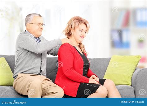 Mature Man Giving Massage To His Wife Seated On Couch Stock Photo