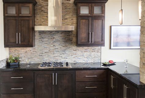 Dark Stained Cabinetry With Glass And Stone Mosaic Backsplash And Black