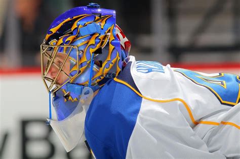 A Hockey Goalie Wearing A Blue And White Uniform With His Face In The Net