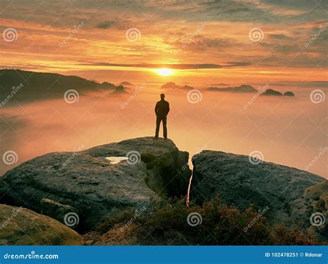 Man Stands Alone On The Peak Of Rock Hiker Watching To Autumn Sun At