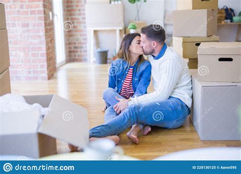 Young Beautiful Couple Sitting On The Floor Kissing At New Home Around Cardboard Boxes Stock