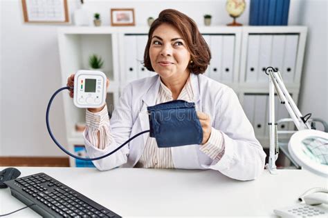 Middle Age Hispanic Doctor Woman Using Blood Pressure Monitor Smiling
