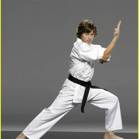 A Man In White Is Doing Karate With His Hands Up And One Leg Bent Out